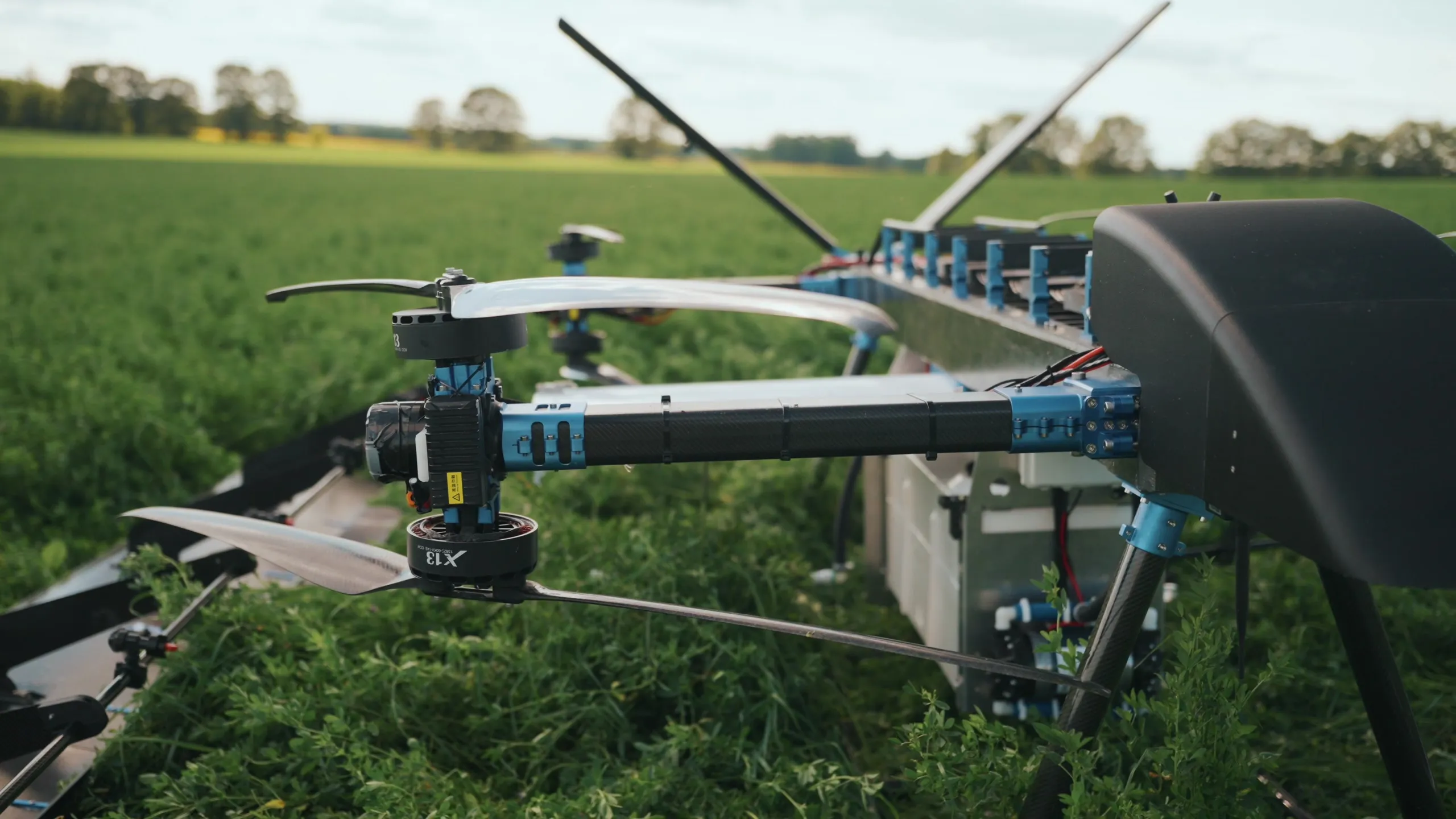 The U9 Spray seen from the front and slightly to one side, standing in crop with its lift rotors above the wing.